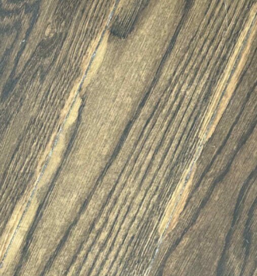 Närbild av ett trägolv med ljusa slipmärken och ojämn yta, pigmentering ser ojämn ut och vissa små håligheter är synliga.