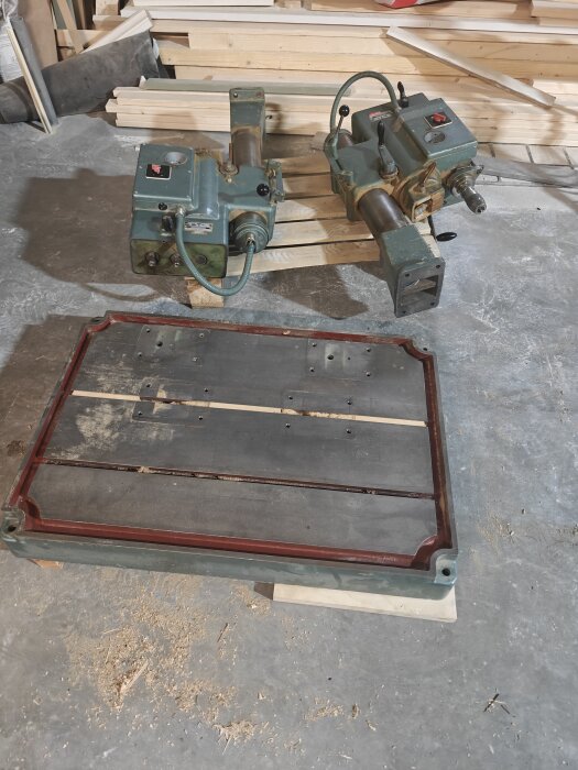 Två sammanlänkade gröna maskiner på träpallar med en bortmonterad basplatta framför, i en verkstadsmiljö.