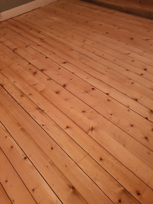 Trägolv med synliga repor och ojämn yta; nyligen skurat, men övervägs för slipning för bättre jämnhet och finish.