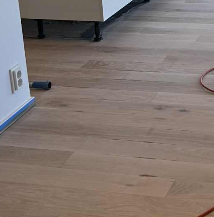 Ljust trägolv med diskreta mörka streck och färgvariationer, resultat av flera slipningar och pigmentering, syns från en sned vinkel.