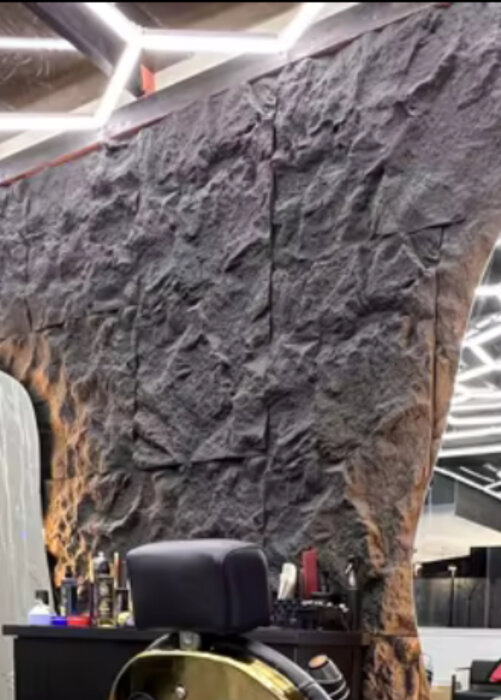 En rustik vägg av texturerad sten med mörka nyanser, mot en bakgrund av modern interiörbelysning och frisörutrustning.