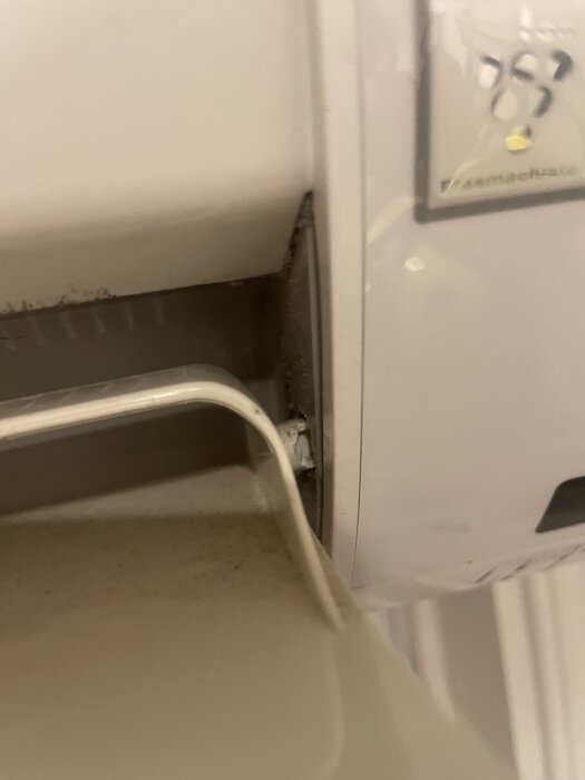 Inre del av luftvärmepump med en skadad vinge; liten plastbit har lossnat från fästet, vilket orsakar problem med vingens rörelse.