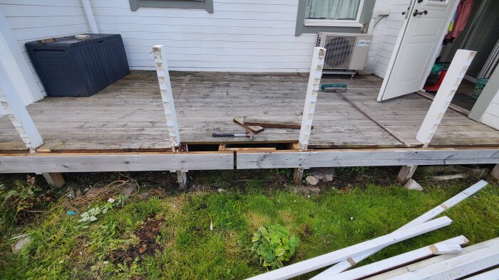 Altan med trasigt räcke, borttagna stolpar, hammare och såg liggande på golvet, grön gräsmatta framför.