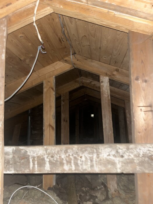 Loft med synliga träbjälkar och elledningar.