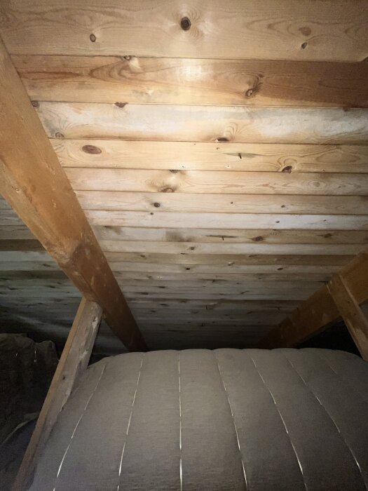 Loftutrymme med träbalkar och råspont i taket, mörk uppblåsbar struktur syns i förgrunden.