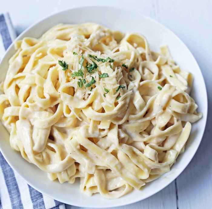 Tallrik med krämig fettuccinepasta toppad med riven parmesan och hackad persilja.