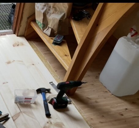 Trappa i hall med verktyg och material liggande på gammalt golv. Planeras att målas och ett förråd byggas under trappan i ett hus från sent 1800-tal.