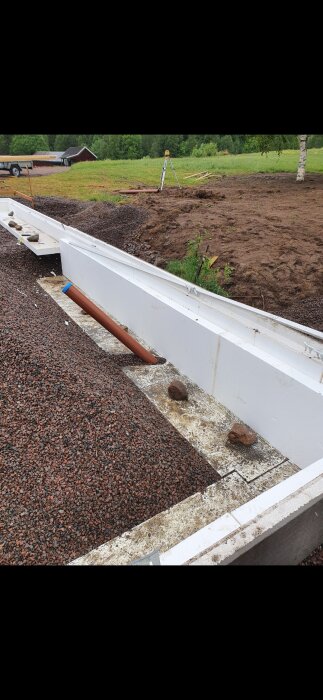 Betonggrund med rör och grus, troligen del av ett byggprojekt med pågående arbete i en utomhusmiljö.