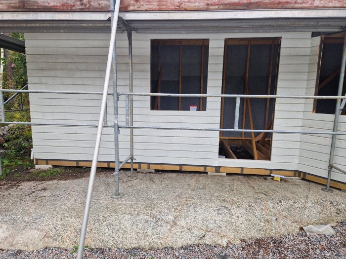 Byggprojekt påbörjat med vitmålad vägg, ställningar och öppen interiör, byggt direkt på berg under hösten.