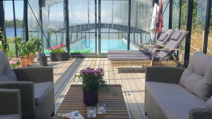 Poolområde med skjutbart tak, loungemöbler och växter. Den angränsande infinity-kanten erbjuder utsikt över havet i soligt väder.