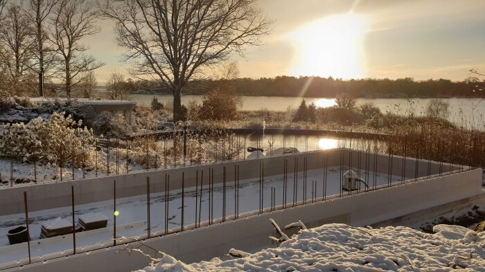 Poolkonstruktion under vintern, termoblock synliga med armeringsjärn. Solnedgång i bakgrunden med snötäckt landskap och sjö.