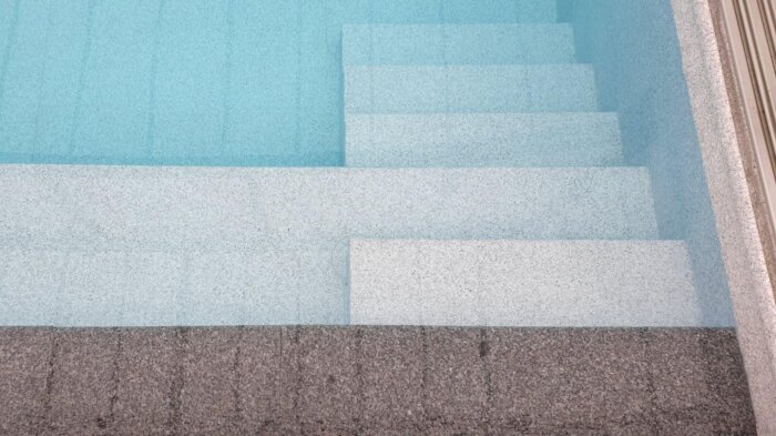 Pooltrappa av ljus sten under vatten, från ovan med gradvis fördjupning i klart vatten.