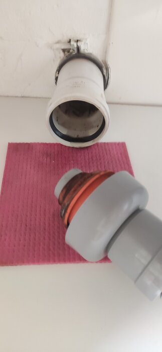 Anslutning avloppsrör med synlig orange o-ring och vit koppling ovanpå en rosa trasa.