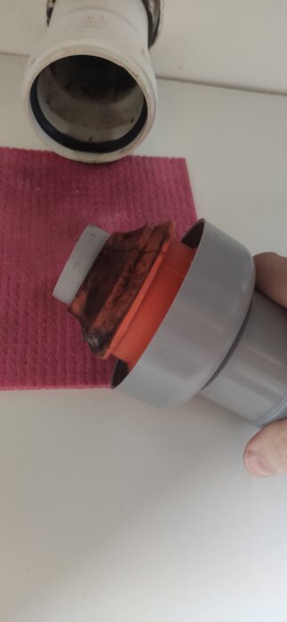 Avloppsrörsanlutning med orange damask och svart o-ring, hålls av en hand över en rosa trasa, visar eventuell läcka efter spolning.