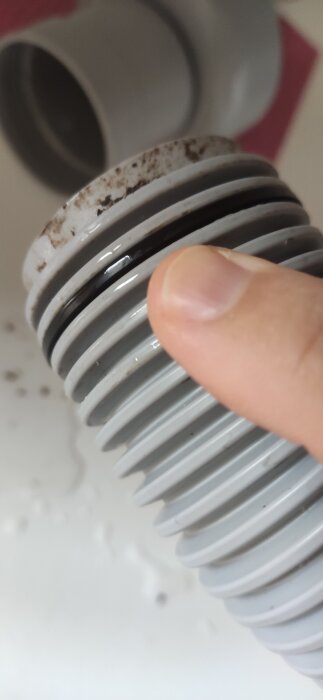 Närbild på en grå slang med en svart o-ring nära en anslutning; en hand justerar positionen på o-ringen.