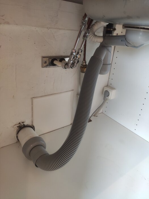 Diskbänkens avloppsanslutning med grå avloppsslang och rör under diskhon, fokus på möjlig läcka vid anslutning.