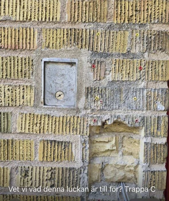 Gul tegelvägg med lucka märkt "FVS" och rustik yta synlig nedanför.