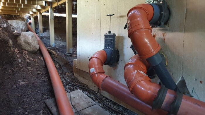 Orange rörsystem och ventiler under ett trädäck, del av poolens uppvärmningssystem med värmepump och isolerande åtgärder.