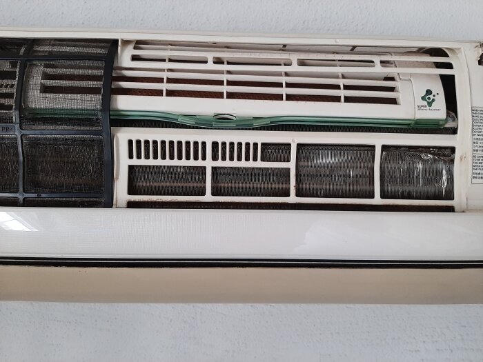 Närbild av en äldre Panasonic luftvärmepump med synliga filter och skadade delar. Filtrena är rengjorda, men enheten ser sliten ut.