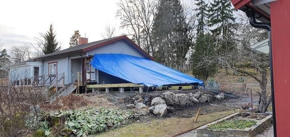 Hus med en blå presenning fastklämd mot fasaden med en bräda, använd som skydd vid renovering.
