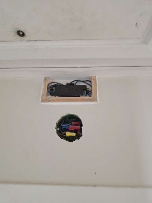 Ett hemmagjort doslock med förhöjningsram ovanför en öppning med synliga elledningar i olika färger, monterat på en vägg eller tak.