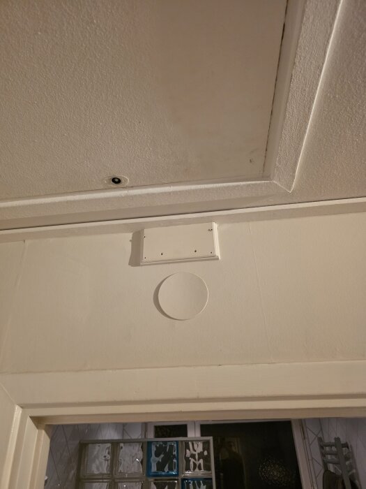 Ett doslock på väggen, kapat på mitten och monterat på en förhöjningsram, ovanför dörrkarmen i ett rum med ljus inredning.