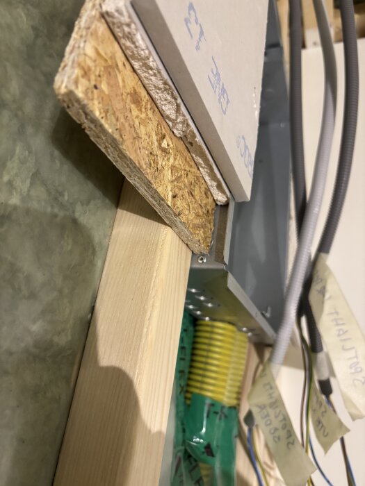 Bottenlåda monterad mot regel, omgiven av gips- och OSB-skivor, samt elledningar med märkta kablar i bakgrunden.
