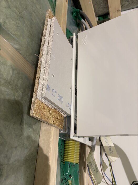 Närbild på osb- och gipsskivor monterade mot träram med synliga kablar och anslutningar för en normcentral i byggprojekt.