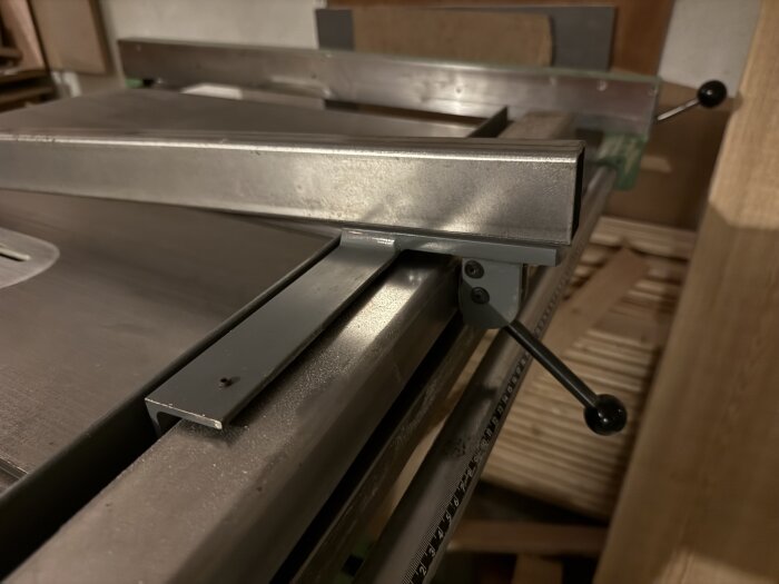 Närbild av en metallkonstruktion på en såg, med justeringsspakar och linjal i bakgrunden.