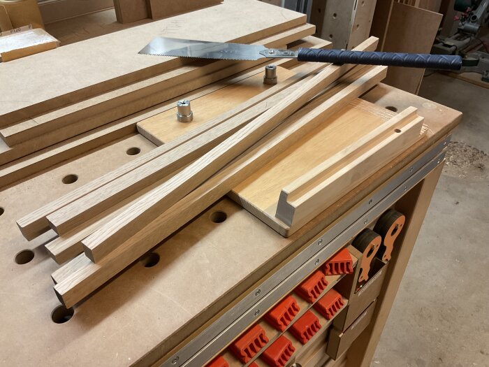 Staplade träbitar på en arbetsbänk för side board-bygge, med en sågs klinga liggande ovanpå.