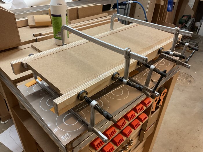 Träprojekt i verkstad: MDF-skivor kantas med eklister och kläms fast med tvingar på arbetsbänk; verktyg och material syns runtom.