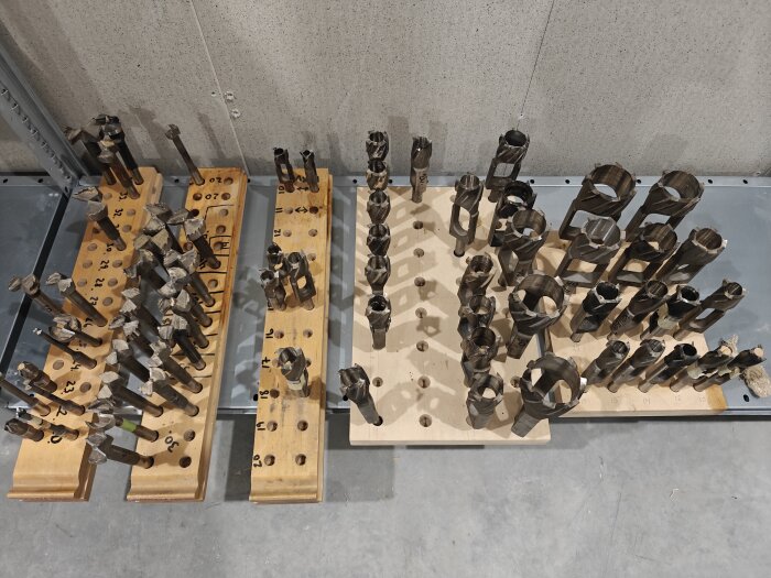 Sortiment av olika borrverktyg organiserade i träställ, med vissa verktyg av olika storlekar och former.