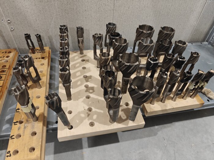 Uppställning av olika stora borrverktyg på träblock, vissa numrerade och placerade på en golvyta av betong.