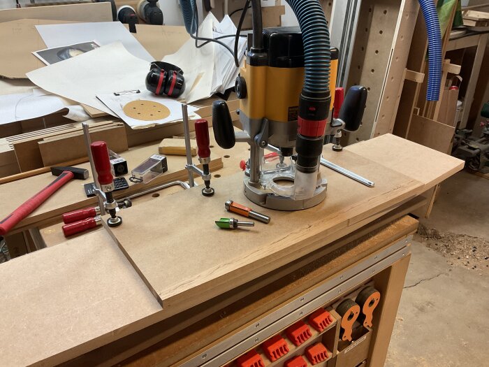 Bearbetning av MDF-skiva i verkstaden med en handöverfräs. Verktyg och diverse material synliga på arbetsbänken.