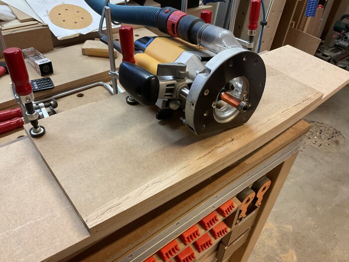 Router på arbetsbänk använd för att fästa kantlister på MDF-skiva. Excenterslip och spännhylsa synliga, verkstadsmiljö i bakgrunden.