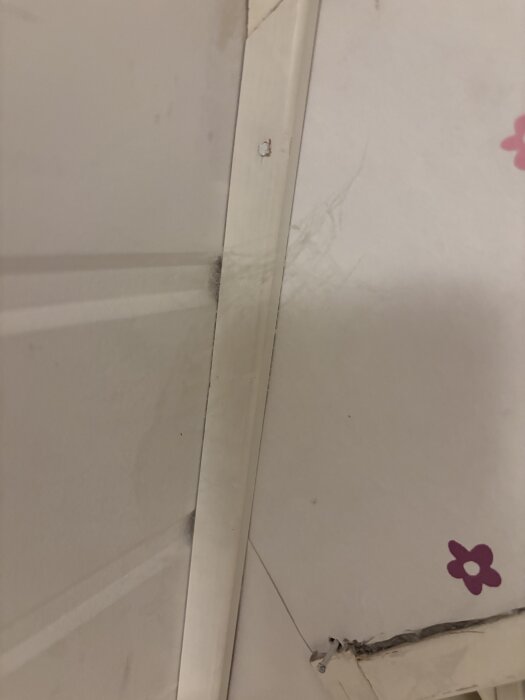 Vitt innertak med otydlig mörk fläck vid taklisten, möjligtvis damm, spindelnät eller mögel. Fläckarnas ursprung är osäkert.