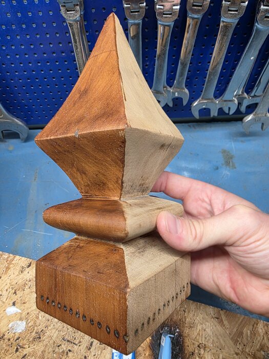 Trädetalj behandlad med bivax, skillnad synlig mellan vänster och höger sida, hålls av en hand, verktyg i bakgrunden.