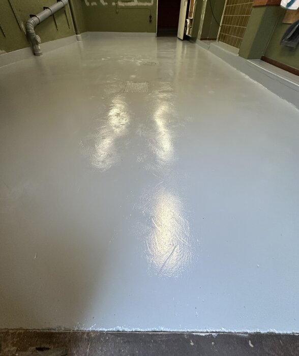 Nymålat och blankt golv med lite ojämn yta, sägs bero på målning med roller. Fönster och garagedörr öppna, avfuktare använd.