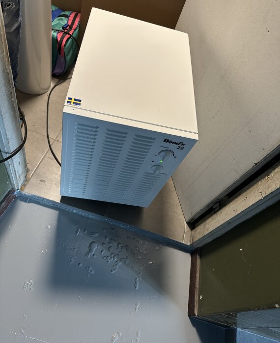 Nymålat golv med ojämnheter och en avfuktare placerad i ett hörn, några fönster är glänt och dörren står på glänt.