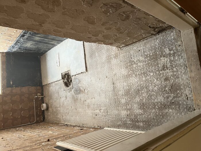 Bild av ett badrumsgolv efter vattenskada, där betongen är blottad och en del av väggen visar rör och fuktfläckar.