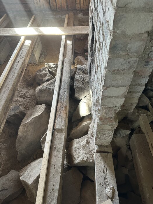 Murstock i ett gammalt hus med synliga stenar och bjälkar kring grunden, i behov av renovering och återställande av kakelugn och vedspis.