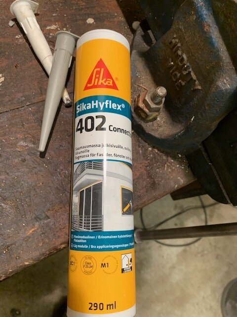 Tuben med fogmassa SikaHyflex 402 Connect ligger på ett arbetsbord bredvid en vit munstycke.