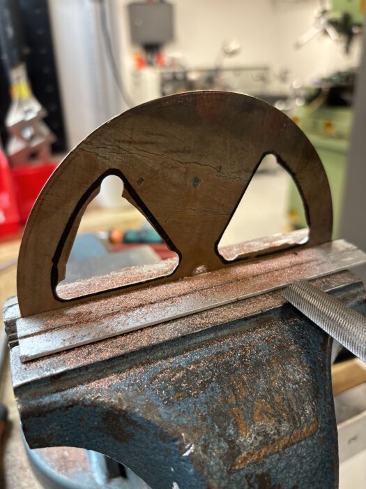 Kopparventildel fastspänd i ett skruvstäd under bearbetning med fil, placerad i en verkstadsmiljö.