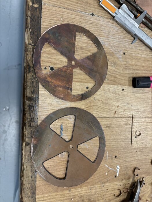 Kopparskivor med ventilutskärningar på arbetsbord, verktyg runtomkring.