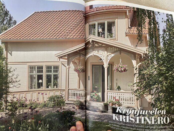 Villa med verandatak och omgivande trädgård. Fönster ovanför verandan; avbildat i tidskrift med titeln "KRISTINERO".
