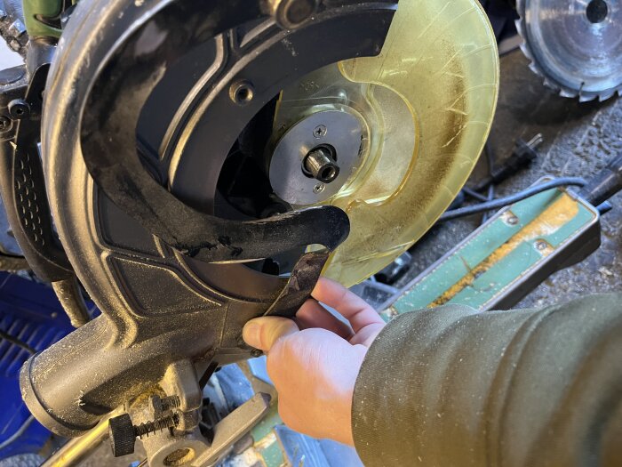 Defekt klingksydd på Hitachi kap- och gersåg c8fse med böjd arm som inte lyfter skyddet korrekt. Hand som pekar på problemet.