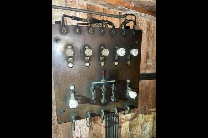 Äldre elcentral med keramiksäkringar och strömbrytare monterad på träpanel, troligen från en hissinstallation från tidigt 1900-tal.