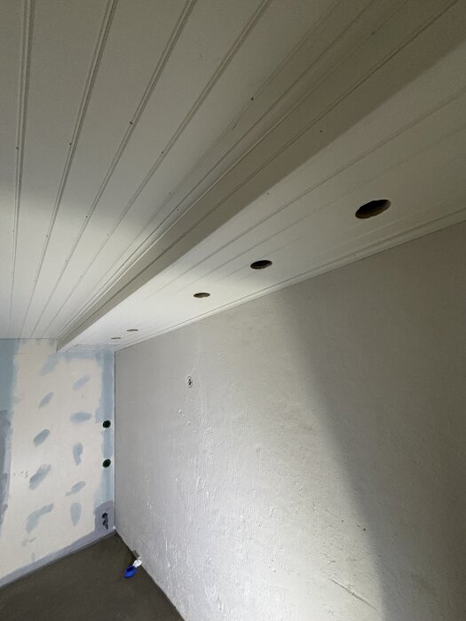 Ett rum med nyligen monterat vitt tak och lister. Väggarna förberedda för målning och kakel, med nedsänkta runda hål för lampor.