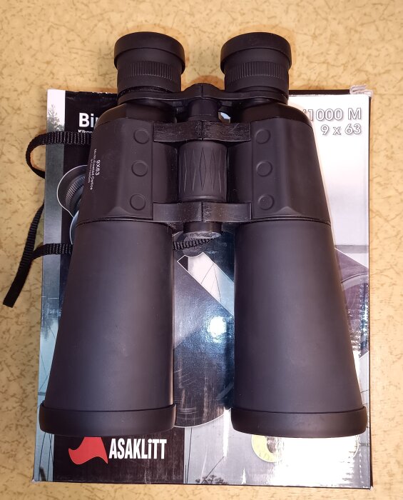 Svarta kikare av märket Asaklitt på ett bord, med halkfri beläggning som orsakat problem vid användning, enligt texten.