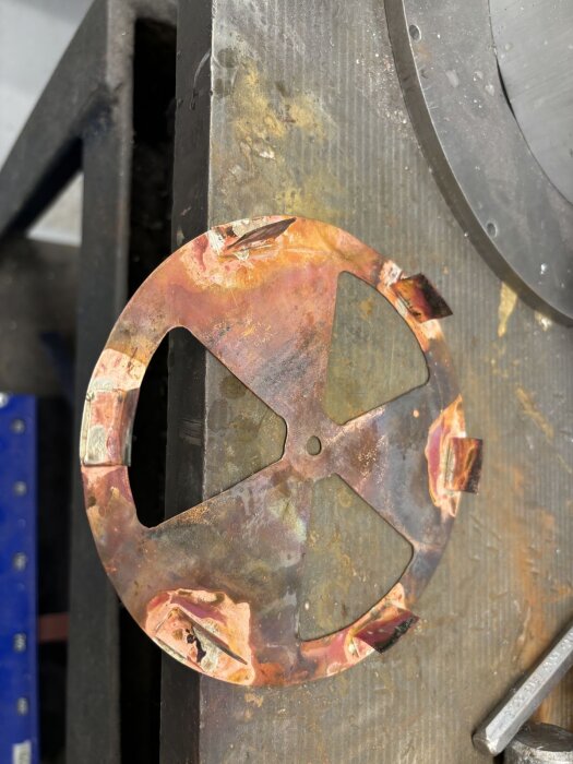 Rund kopparplåt med utskurna sektioner och vikta kanter, placerad på ett arbetsbord för ventilationsventil-projekt.